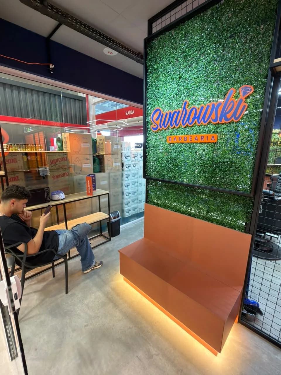 Área de espera com o muro verde e o letreiro da Swarowski Barbearia