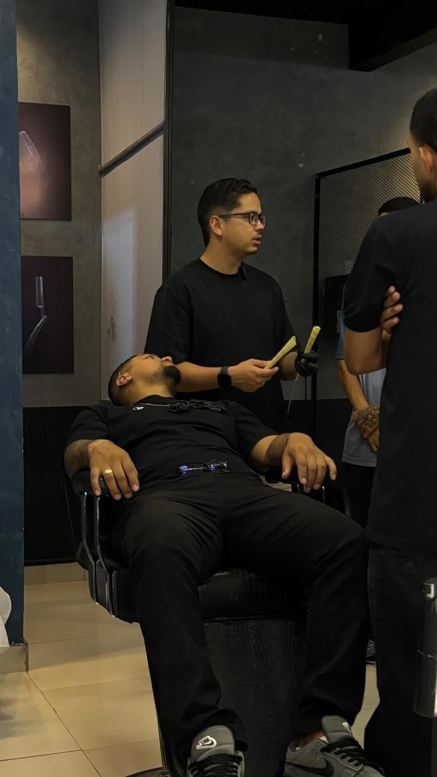 Lucas Alcântara, de luva e com cones de cera nas mãos, orienta a turma ao lado do cliente reclinado na cadeira