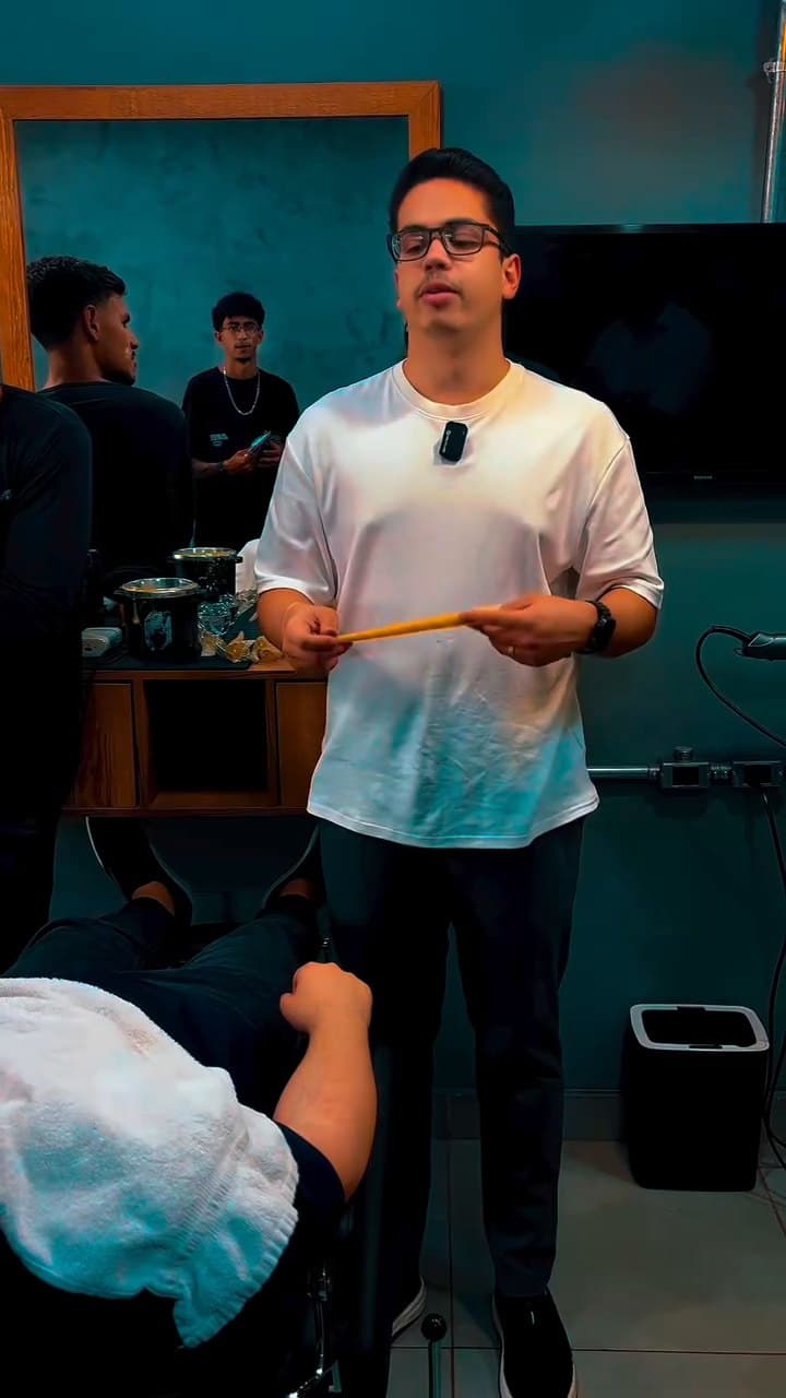 Lucas Alcântara em pé conduzindo a prática de serviços extras, com a turma acompanhando dentro da barbearia